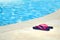 Pink flip flops near the swimming pool with blue water. Summer vacation in tropical resort. Beach shoes. Pair of thong sandals