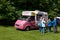 Pink Ford Transit van in a green park providing ice cream to customers in a queue
