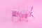 Pink Friday concept. Funny pink dinosaur toy with shopping cart full of present boxes on pink background
