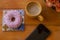 Pink frosted donut on the wooden table, coffee cup and cellphone - pause or breakfast