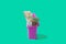 A pink garbage can full of different paper banknotes against green background. Surreal creative concept for waste of money