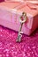 Pink gift box with ribbon bow and golden love key in the foreground on abstract glitter bokeh