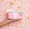 Pink gift with falling confetti. Minimal background composition with hand holding gift on pastel pink