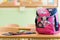 Pink girly school bag and pencil case on a desk in an empty classroom.