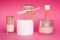 Pink glass perfume bottles, facial cream and some cosmetic and makeup products on pink background. Bottle of female