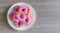 Pink glazed mini donuts in white plate on wooden table. Sweet food background