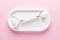 Pink Guasha massage tool on white concrete tray on pink background. Rose quartz jade roller. Skin care at home, anti-aging and