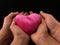 Pink heart on the palms of a woman and a man. Two pairs of hands hold a heart, on a black background. Concept: take care of love,