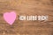 Pink heart post-it with the text `Ich liebe dich`on a wooden background. Translation: `I love you`