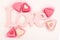 Pink heart shaped petit fours cakes seen from above decorated around pink letters stating Love