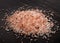 Pink Himalayan coarse grain salt on black stone background.