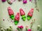 Pink homemade fruits and berries ice cream or popsicles on teal rustic green table background, decorated with garden flowers