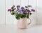 pink jug with a purple bouquet of ageratum.