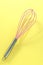 Pink kitchen whisk on yellow background