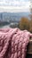 Pink knitted scarf on a wooden table with a view of the city