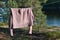 A pink knitted sweater is drying on a rope in the forest among the trees.