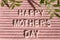 Pink letterboard with quote Happy Mother`s Day, decorated with green leaves on pink background