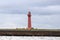 A pink lighthouse on the bay in cloudy weather