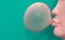 A pink mannequin with a female face inflates a bubble of chewing gum. Pink bubble gum on a turquoise background. Creative