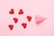 Pink menstrual cup and red hearts as blood drops isolated on rose background, menstruation cycle, women gynecological health and