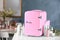 Pink mini cosmetics refrigerator and skin care products on white table