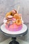 Pink and orange birthday cake decorated with macaroons, meringues, donuts, waffle cones, cake pops and chocolate bars.