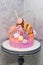 Pink and orange birthday cake decorated with macaroons, meringues, donuts, waffle cones, cake pops and chocolate bars.