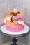 Pink and orange birthday cake decorated with macaroons, meringues, donuts, waffle cones, cake pops and chocolate bars.