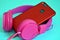 Pink overhead external large headphones and a phone with a dual camera in a red protective case. Closeup on a blue background.