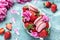 Pink peony rose flower and macaroni cookies and sweet strawberry on blue background. Small French cakes Macarons with fruit. top