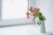 Pink peony tulips in a white jug stand on the window.