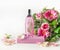 Pink perfume glass spray bottle on podium with beautiful flower bouquet at white background.  Front view