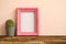 Pink photo frame on old wooden table with cactus over pink wall