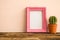 Pink photo frame on old wooden table with cactus over pink wall