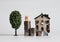 A pink pig on three pile of stepped coins in front of a miniature house with a miniature tree.