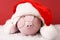 Pink piggy bank with Santa hat with pompom and glasses standing on white snow on red background