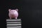 Pink piggy bank on top of stack of books with dark blackboard or chalkboard background using as cost of knowledge and education,