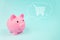 Pink piggy bank with trolley digital hologram in cloud thought above his head on blue background