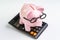 Pink piggy bank wearing glasses on black calculator on white background using as education budget, cost or investment calculation