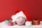 Pink piggy box wiht glasses and santa hat with pompom and three gift boxes with ribbon standing on white snow on red background