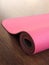 Pink pilates, yoga or fitness mat on wooden floor.