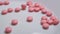 Pink pills fall down on white background in slow motion