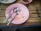 Pink plastic dish, spoon and fork steel are table wooden with copy space