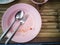 Pink plastic dish, spoon and fork steel are table wooden with copy space