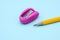 Pink plastic pencil sharpener and a yellow pencil on blue.