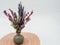 Pink and Purple artificial wildflowers in a gray ceramic vase sitting on a round pink and white placemat with a white background