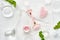 Pink quarts face roller, gua sha stone, pink cream in glass jar. Off white flat lay in green and pink with ice and