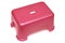 A pink red plastic stool with four short leg supports