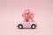 Pink retro toy car delivering bouquet on pink background. February 14, Valentine`s day.. 8 March, International Happy Women`s Day.