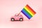 Pink retro toy car delivering bright rainbow gay flag on the soft pink backgraund. Concept of gay parade, LGBT community, adoption